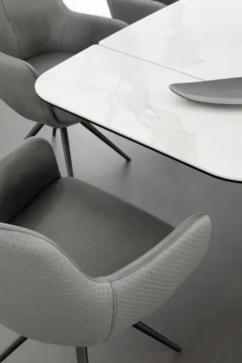 Ansicht eines grauen Design Armlehnstuhls, der auf der Rückseite mit Stoff und innen mit Leder bezogen ist und an der Stirnseite eines weißen Designer Esstisches steht.
