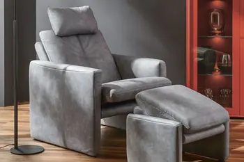 Grauer Ledersessel mit passendem Fußhocker davor in einem modernen Raum.