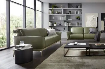 Olivegrünes Ledersofa mit umgeklappten Kopfstützen und silbernen Beinen neben einem weiteren grünen Ledersofa und einem grünen Ledersessel in einem hellen modernen Raum mit großen Fenstern.