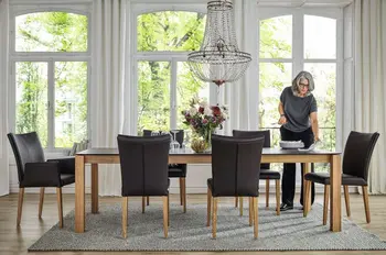 Großer Massivholz Esstisch mit schwarzer Tischplatte, an dem eine Frau steht und den Tisch deckt.