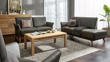 Ein braunes Ledersofa mit Holzbeinen neben einem weiteren braunen Ledersofa mit Recamiere in einem gemütlichen Wohnzimmer.