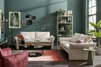 Zwei beige Sofa Garnituren mit großen Rückenkissen vor einer grünen Wand.