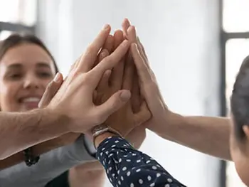 Eine Gruppe von Leuten hält die ausgestreckten Hände in der Luft zusammen.&nbsp;