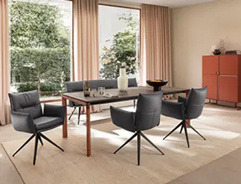 Edel eingerichtetes Esszimmer mit großem Holztisch, Armlehnstühlen und Bank in dunklem Leder.