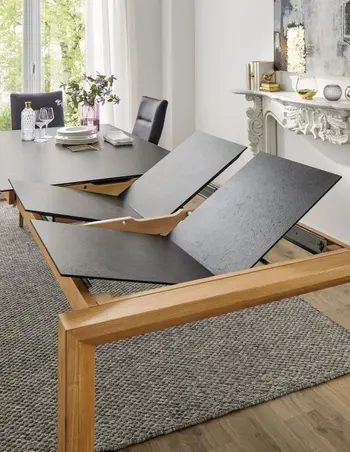 Esstisch mit schwarzer Tischplatte an dem zwei weitere Tischplatten zur Verlängerung angebracht werden.