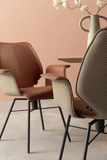 Zwei sich gegenüberstehende Armlehnstühle mit schwarzem Metallfußgestell und außen beigem Stoffbezug und innen mit Leder bezogen in rose.