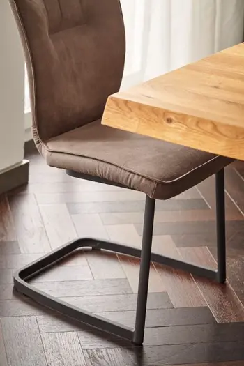 Freischwinger mit braunem Leder und schwarzem Metallgestell, der an einem Esstisch steht.