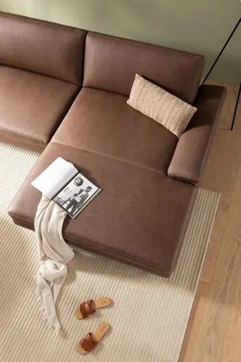 Braunes Leder Ecksofa dekoriert mit beigem Kissen und Decke sowie einer Zeitschrift.