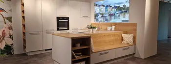 Weiße Küche mit Holzarbeitsplatte und Kücheninsel mit integrierter Sitzgelegenheit.