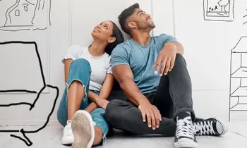 Ein Paar sitzt auf dem Boden und schaut nach oben, im Hintergrund sind Umrisse von Möbeln auf die Wand gemalt.&nbsp;