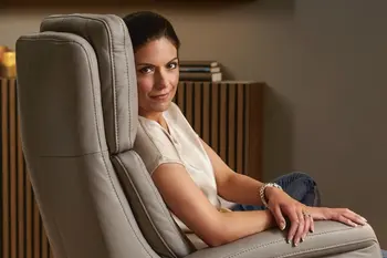 Dick gepolsterte Rückenlehne eines hellbraunen Relaxsessels, in dem eine Frau sitzt.