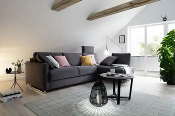 Graues Ecksofa mit dem Longchair auf der rechten Seite, auf dem Sofa sind mehrere Kissen dekoriert in weiß, rosa und gelb.