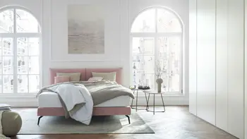 Altbauwohnung mit hohen Decken und großen Fenstern in dem ein rosa Design Polsterbett steht.