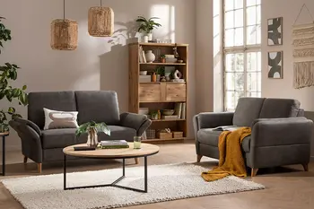 Gemütliches Wohnzimmer mit zwei Zweisitzer-Sofas in dunklem Grün, rundem Couchtisch und Regal aus Massivholz.