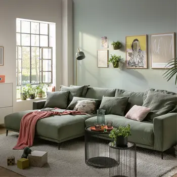 Grünes Ecksofa mit Kissen im Wohnzimmer neben Sideboard