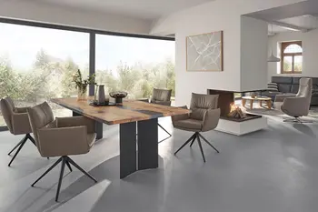 Halboffener Essbereich in einem sanierten Bauernhaus mit Massivholz Esstisch und drehbaren grauen Armlehnstühlen. 