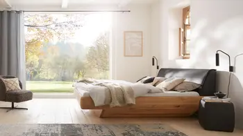 Helles Schlafzimmer mit Doppelbett aus Massivholz und mit gepolstertem Lederkopfteil, passenden Nachttischen und Loungesessel.