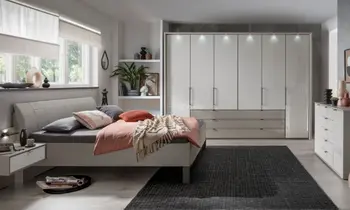 Sie sehen ein Schlafzimmer mit Drehtürenschrank, großen Schubladen mit passendem Bett und Kommode in Glasfront hell mit Kranzbeleuchtung