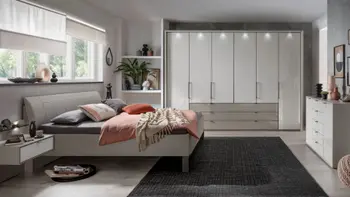 Helles Schlafzimmer mit einem weißen Bett, großen Kleiderschrank, Kommode und Nachttisch.