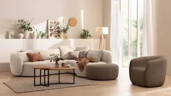 Beiges Sofa in organischer Form mit angrenzendem Hocker in braun und passendem Sessel in braun in einem hellen gemütlich dekorierten Wohnzimmer mit vielen Pflanzen.