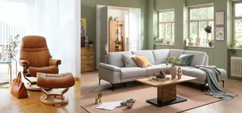 Brauner Relaxsessel mit Bezug aus Leder und hellgraues Ecksofa mit hoelzernem Couchtisch in Wohnzimmer.