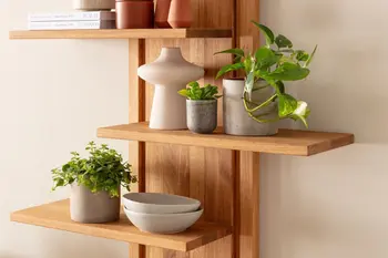 Zeitloses Wandregal aus hellem Massivholz aus Eiche mit versetzten Regalböden, auf denen Pflanzen, Vasen und schalen in grau und beige stehen.