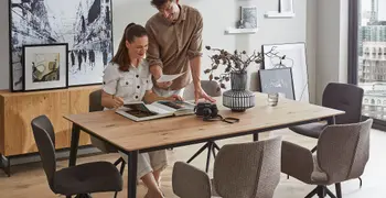 Moderner Esstisch mit Massivholztischplatte und schwarzem Gestell und grauen Schalenstühlen, die um den Tisch stehen.