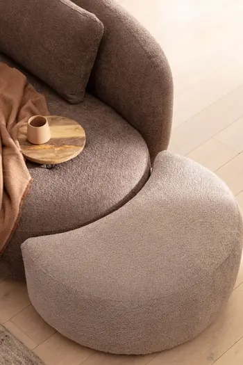 Braunes Sofa mit rundung, an dessen rechter Seite ein passender runder Hocker in creme steht.