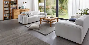 Zwei graue Sofas mit runden Ecken die sich gegenüber stehen und mit Kissen und einer Decke dekoriert sind.