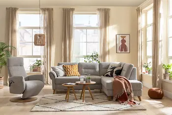 Graues Ecksofa mit bequem gepolsterten Rückenpolster und zwei Kopfstützen neben einem grauen Relaxsessel in einem gemütlichen Wohnzimmer.