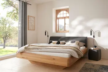 Harmonisches Schlafzimmer eines Bauernhauses mit Doppelbett aus Massivholz und gepolstertem Kopfteil mit Lederbezug.