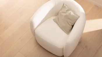 Gemütlicher weißer Boucle Sessel mit einem beigen Kissen, der von der Sonne gestreift wird.