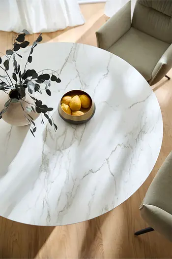 Runder Esstisch mit Keramiktischplatte in Marmoroptik dekoriert mit Vase und Dekoschale mit Zitronen.