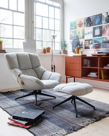 Grauer Stoffsessel mit Fussauflage vor rotem Sideboard