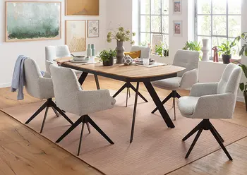 Moderner Essbereich mit Massivholztisch in Eicheoptik und schrägen Metallbeinen, umgeben von sechs gepolsterten, drehbaren Armlehnstühlen in hellem Stoff – stilvoller Esszimmer-Look mit gemütlichem Ambiente und viel Tageslicht.