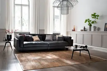 Helles Wohnzimmer in dem ein modernes Ledersofa mit schwarzem Bezug steht, das Sofa ist mit vielen Dekokissen dekoriert in den Farben grau, beige, rot.