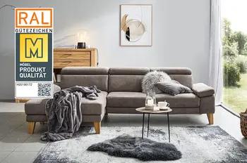 Siegel "Goldene M" auf einem Bild von einem Braunen Ecksofa mit klappbaren Kopfstützen und Armlehnen in einem hellen Wohnzimmer mit großem Fenster.