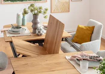 Ausziehbarer Esstisch mit Synchronauszug in Massivholzoptik, zeigt integrierte Einlegeplatte in Funktion – elegante Erweiterungslösung für moderne Essbereiche mit gemütlichen Stoffstühlen und stilvoll gedecktem Tisch.