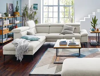 Weisses Stoffsofa mit hoelzernem Couchtisch in gemuetlichem Wohnzimmer mit Kissen und Decke.