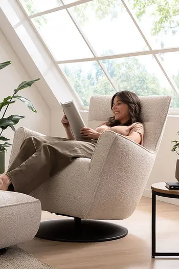 Frau lehnt sich entspannt in beigem Sessel mit Kippfunktion zurück und liest eine Zeitschrift.