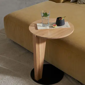 Runder Beistelltisch aus hellem Holz, der an einem gelben Daybed steht. 