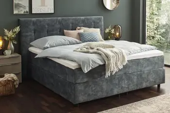 Graues Boxspringbett mit rautensteppung am Kopfteil in einem hellen Schlafzimmer.