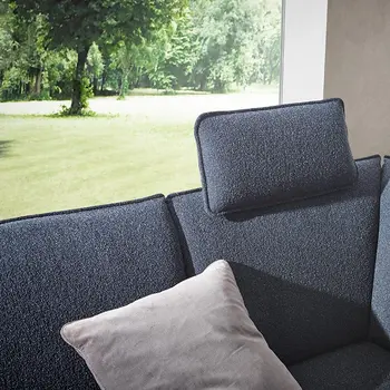 Blaues Ecksofa mit einem Kissen als Kopfstütze vor einem großen Fenster im Hintergrund mit Blick ins Grüne.