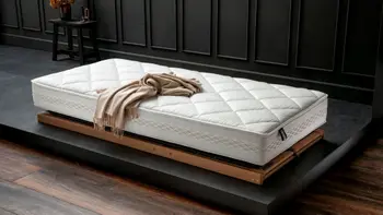 Hochwertige Matratze mit Rautensteppung, die auf einem Lattenrost auf dem Boden liegt, auf der Matratze liegt eine beige Wolldecke.