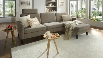 Helles Wohnzimmer mit grauem funktionalen Ecksofa und zwei runden Beistelltischen. 