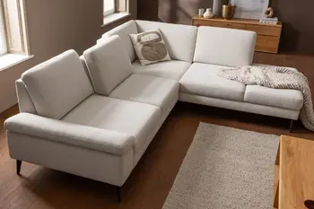 Hellbeiges Ecksofa mit verstellbaren Rückenkissen, dekoriert mit einer beigen Decke und einem Beige-braunen Kissen.