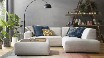 Modernes beiges Ecksofa mit Cordstoff bezogen und einem passenden Hocker, auf dem Sofa sind mehrere Kissen in blau und gelb.