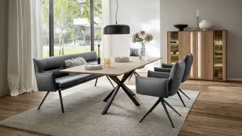 Modernes Esszimmer mit einem Holz Esstisch, um den eine Sitzbank mit Armlehne und schwarzem Fußgestell und dazu gehörige Armlehnstühle in dunkelgrauem Leder stehen.