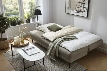 Graues Schlafsofa, das zum Bett umgebaut ist und mit Bettzeug bedeckt ist.