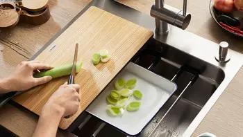 "Person schneidet Lauch auf einem Schneidebrett über einer Spüle, darunter eine Sch